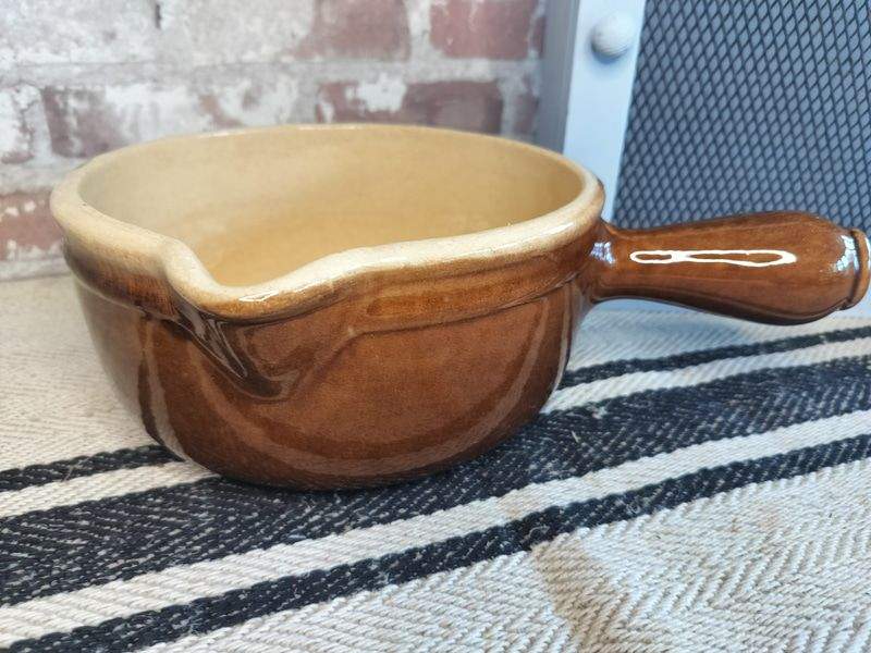 Vintage French glazed brown stoneware skillet casserole pan with handle on striped fabric surface